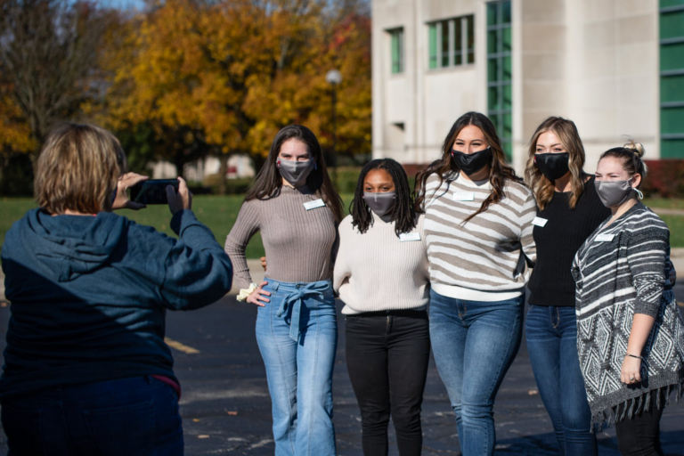 Masked students standing with arms around each other, getting their picture taken in parking lot on IUSB's campus